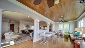 Un salon spacieux doté d’un parquet en bois, un coin repas avec des chaises transparentes et une cuisine en arrière-plan.