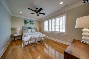 Une chambre à coucher comprenant un lit, un bureau, une chaise, un ventilateur de plafond et une fenêtre avec des stores.