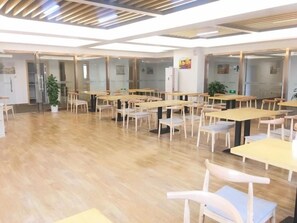 Un vaste espace dédié à la salle à manger, avec de nombreuses tables et chaises, un plancher en bois et des cloisons en verre.