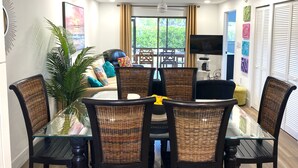 A dining area with a glass table and wicker chairs, a sofa with colorful cushions, and a TV on the wall. - Minutes to Sanibel with Heated Pool, Tennis & Beach Gear (Fort Myers)