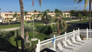 A residential area with a row of two-story buildings, palm trees, and a white fence with lounge chairs. - Minutes to Sanibel with Heated Pool, Tennis & Beach Gear (Fort Myers)