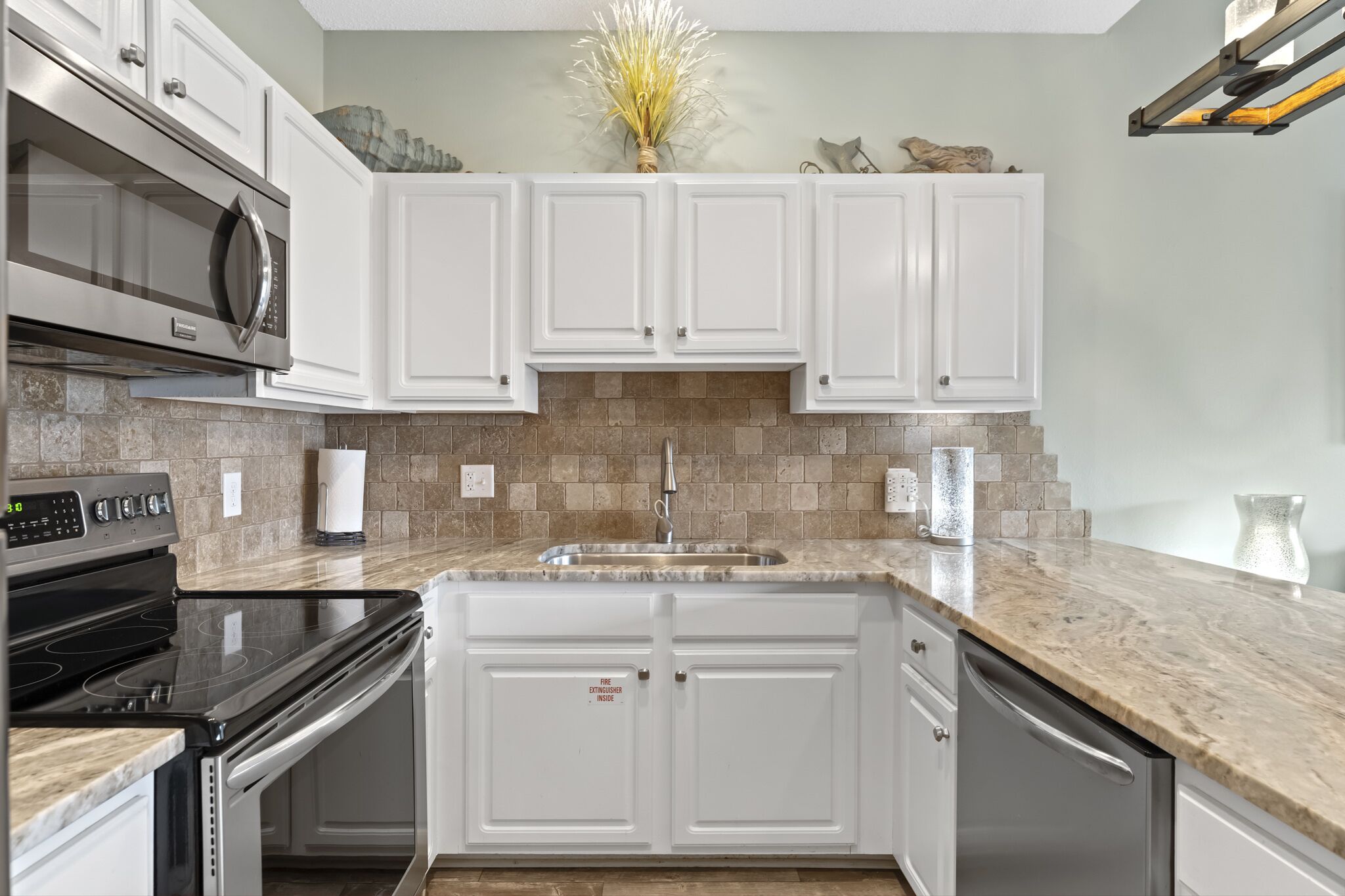 Una cocina moderna con armarios blancos, encimera de granito, electrodomésticos de acero inoxidable y un jarrón decorativo en la pared.