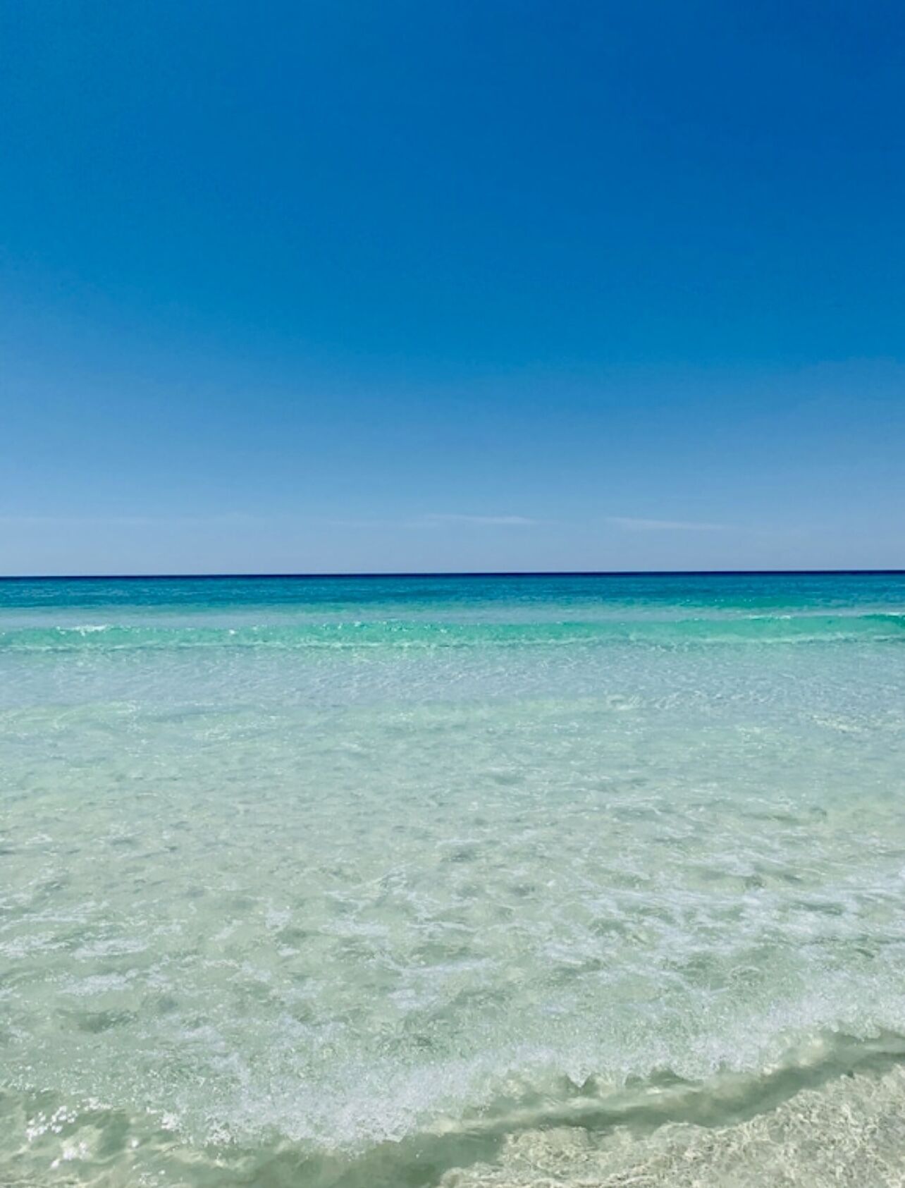 Ein freier Blick auf einen Strand mit türkisblauem Wasser und wolkenlosem Himmel.