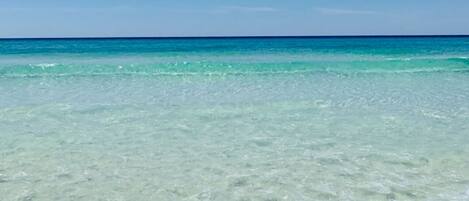 Ein freier Blick auf einen Strand mit türkisblauem Wasser und wolkenlosem Himmel.
