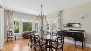 A dining room with a wooden table and chairs, a chandelier, and large windows with curtains. - A historic treasure in Southern Maine, very unique and spacious   (Biddeford)
