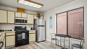 Una cocina compacta con electrodomésticos modernos, un comedor con sillas de metal y un amplio ventanal con vistas.