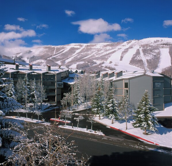 Un pueblo cubierto de nieve en la montaña, con edificios, un río y una pista de esquí al fondo.