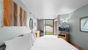 Ein Hotelzimmer mit einem großen Bett, einem Schreibtisch mit Stuhl, einem Fernseher und einem Fenster mit Blick auf eine Straße und Grünflächen.