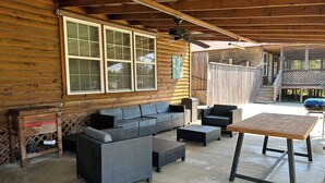 Un espace extérieur abrité, aménagé avec des meubles en osier, une table en bois et un barbecue.