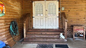 Une cabane en bois avec une porte à deux battants, un paillasson et une petite statue de chien.