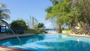 A swimming pool with lounge chairs and palm trees, surrounded by a clear blue sky. - Penthouse villa on the beach, chef services available- extra cost.  (Ocho Rios)