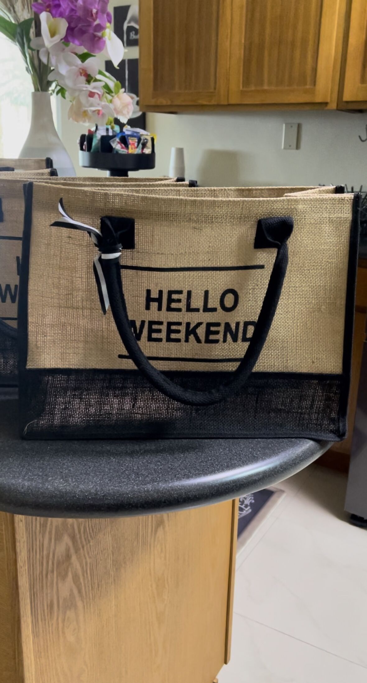 A beige tote bag with black handles and the text "HELLO WEEKEND" on a kitchen counter.