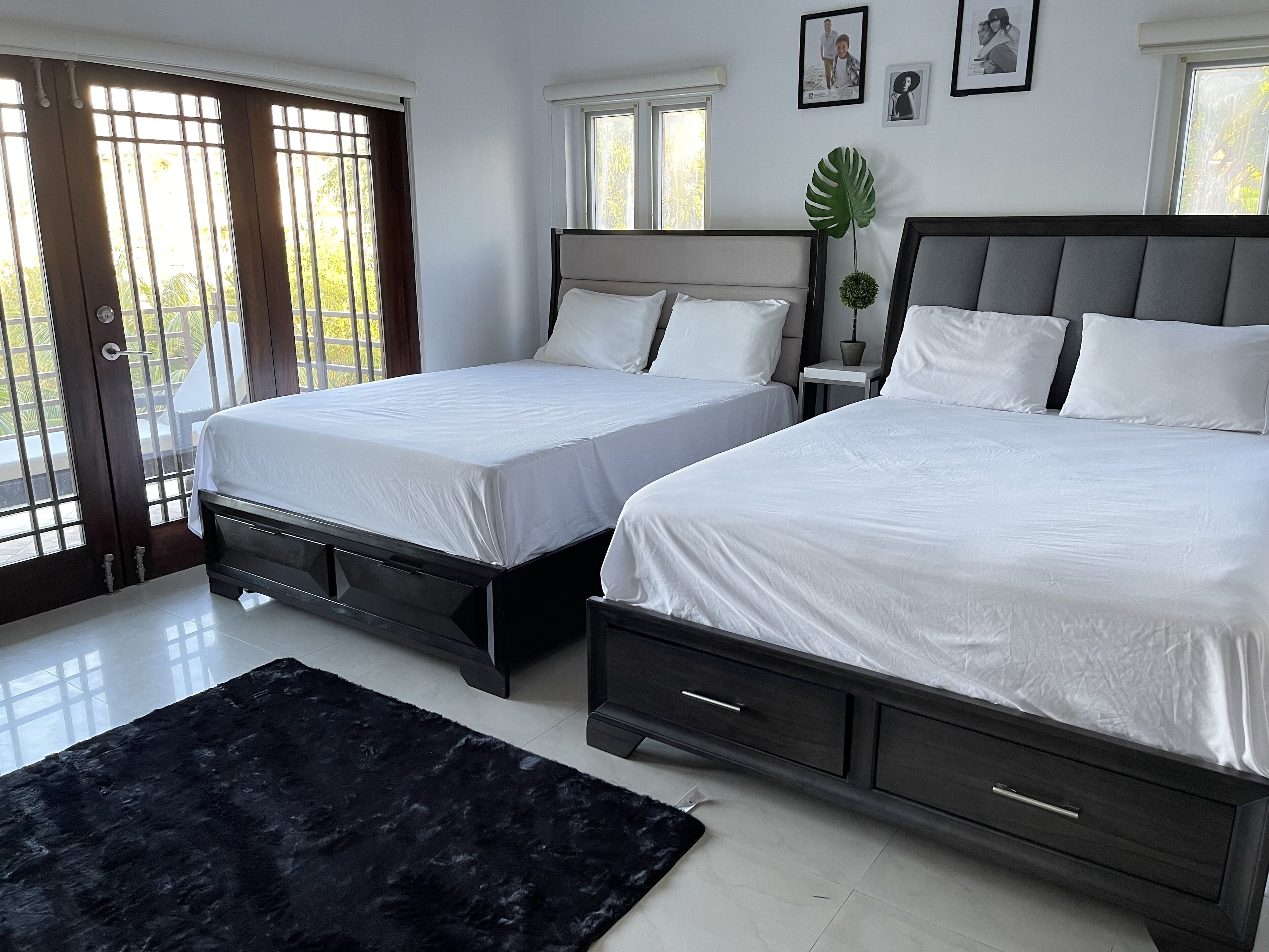 A hotel room with two beds, a black rug, and a view of the outdoors through large windows.