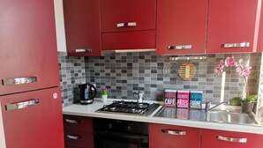Une cuisine avec des placards rouges, une cuisinière à gaz, une machine à café et un évier.