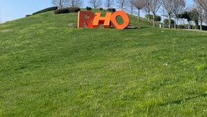 Une colline verdoyante sur laquelle sont disposées de grandes lettres orange formant le mot « RHO ».