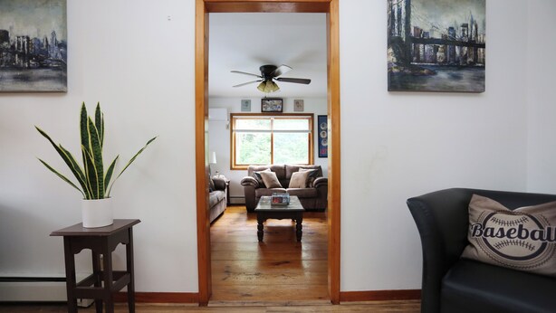 Una sala de estar con piso de madera, ventilador de techo, sofá, mesa de centro y planta en maceta.
