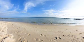 Une plage où l’on peut voir des empreintes de pas dans le sable, une jetée qui s’avance dans l’eau et un ciel dégagé.