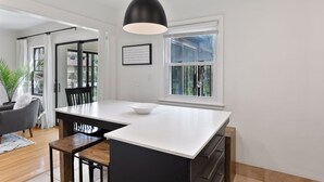 Eine moderne Küche mit einer zentralen Kochinsel, schwarzen Pendelleuchten und Blick ins Freie durch ein Fenster.