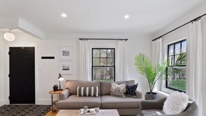 Ein modernes Wohnzimmer mit grauem Sofa, einem Couchtisch und einem großen Fenster mit Vorhängen.