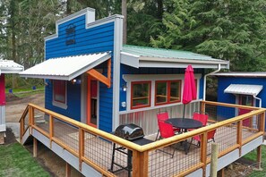 A small, blue cabin with a deck and outdoor seating area.