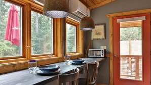 A kitchen with wooden countertops, a dining table with chairs, a microwave, and large windows with a view of trees. - The Ridge at Langley: Villa Oscar (Langley)