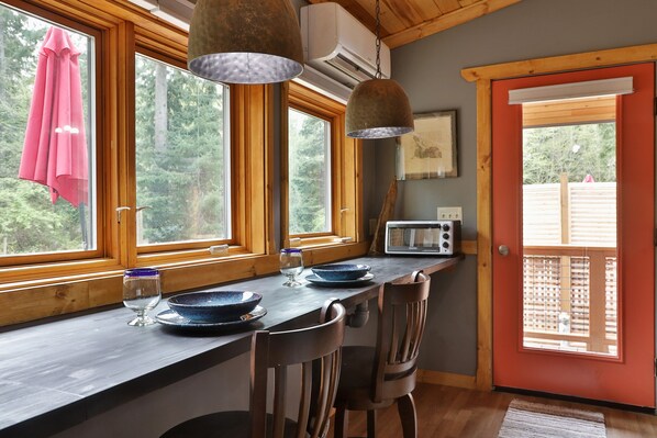 A kitchen with wooden countertops, a dining table with chairs, a microwave, and large windows with a view of trees.