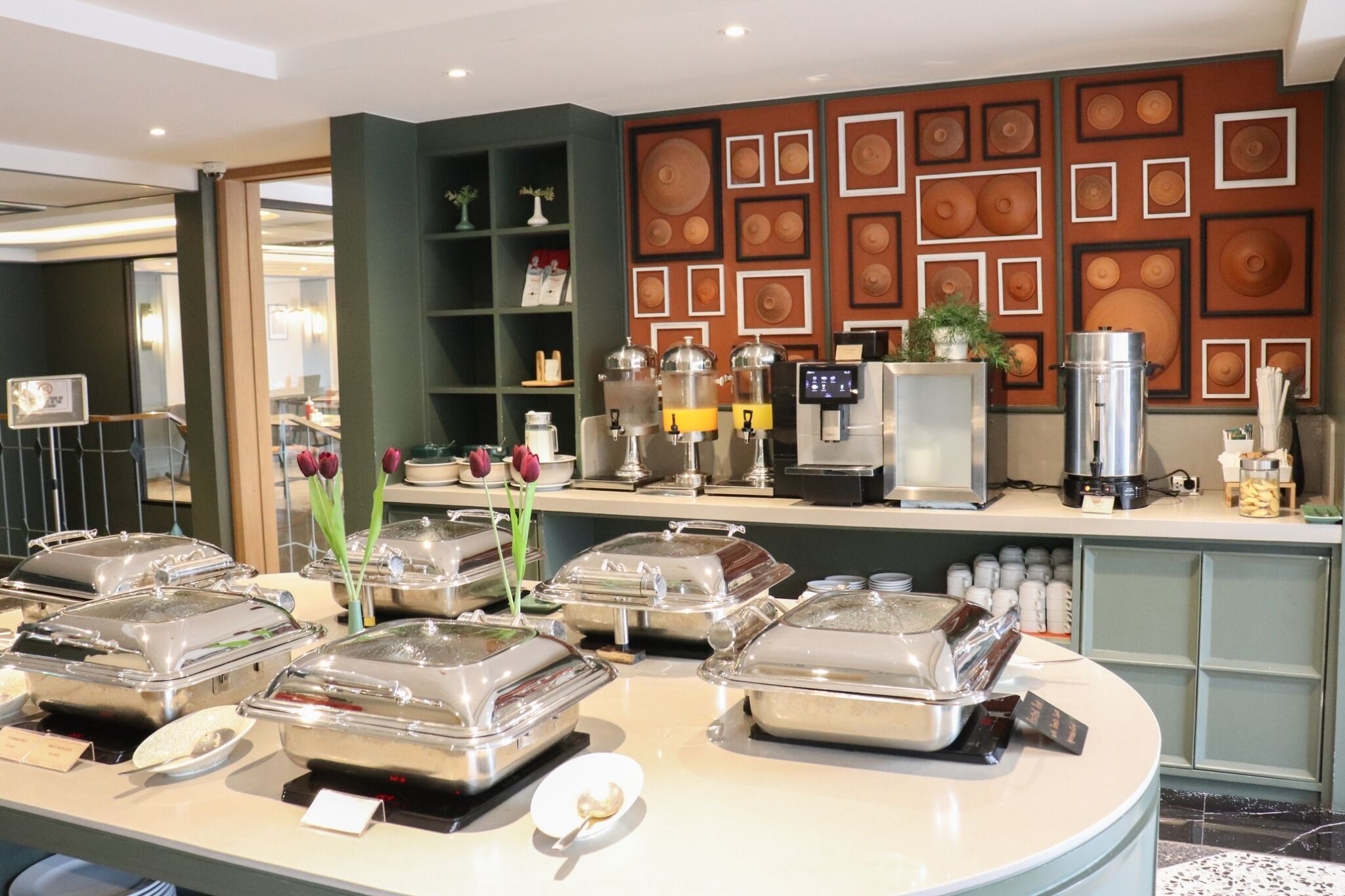 Montaje de bufé con recipientes para alimentos cubiertos, una cafetera y una pared decorativa con diseños geométricos.