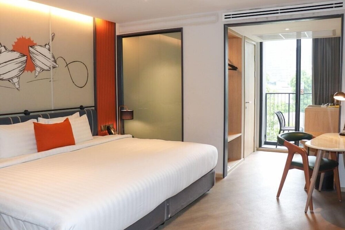 A hotel room with a large bed, a desk with a chair, and a balcony with a view.