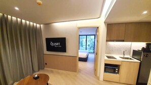 Een moderne woonkamer met een flatscreen televisie, een houten bijzettafeltje en uitzicht op de slaapkamer.