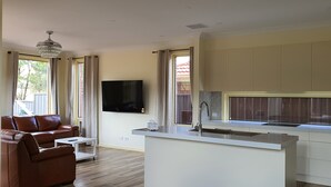 A modern living room with a brown leather sofa, a small white table, and a TV mounted on the wall. - Stylish house in the middle of the Links Lady Bay Golf Course (Normanville)