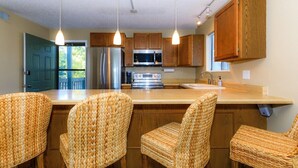 A kitchen with wooden cabinets, a stainless steel refrigerator, a microwave, and a built-in oven. There are four woven chairs around a central island.