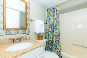 A bathroom with a sink, mirror, toilet, and shower curtain.