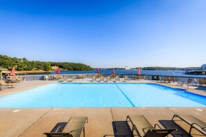 A swimming pool with lounge chairs and umbrellas, surrounded by a waterfront view.