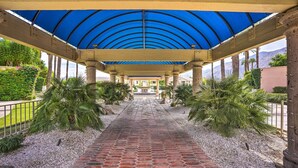 Un porticato con pavimento in mattoni decorati, circondato da palme e vista libera su una catena montuosa all'orizzonte.