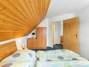 Quarto com teto inclinado, guarda-roupa de madeira e duas camas com roupa de cama estampada.