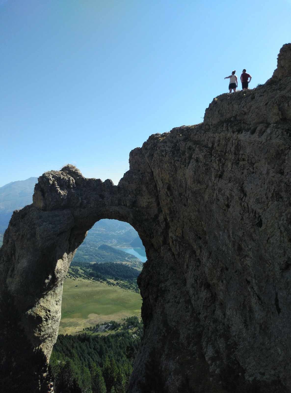 Una formación rocosa arqueada natural con vista a un valle y montañas distantes.