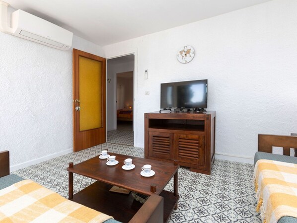 A compact room with a wooden table, a television on a wooden stand, and patterned floor tiles.