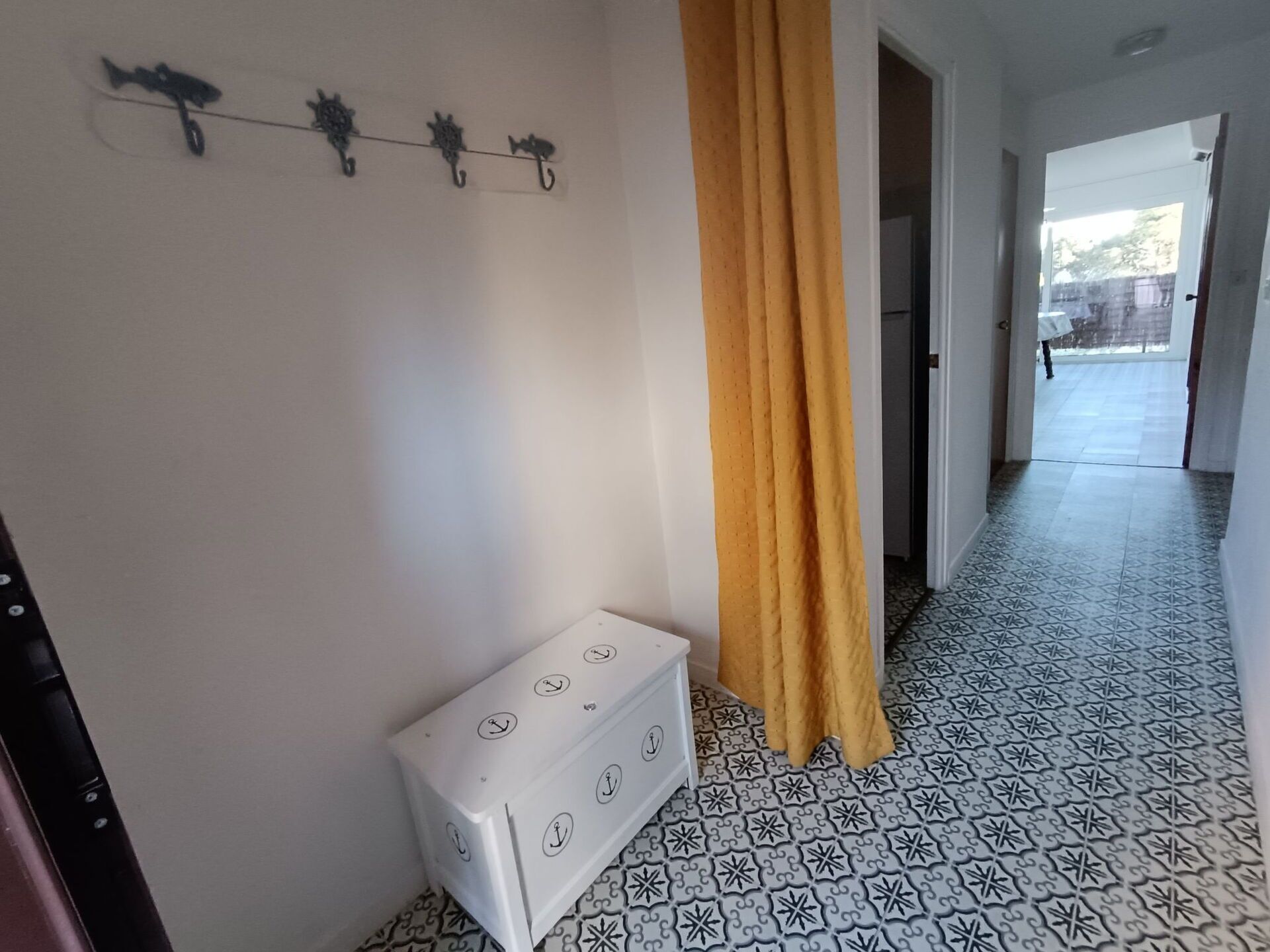 Un pasillo con baldosas de diseño, un aparador blanco, una cortina amarilla y una lámpara fijada a la pared.