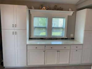 A kitchen with white cabinets, a window with blinds, and a shelf with decorative items. - Holiday House · Lakeview House on Rye Beach (Huron)