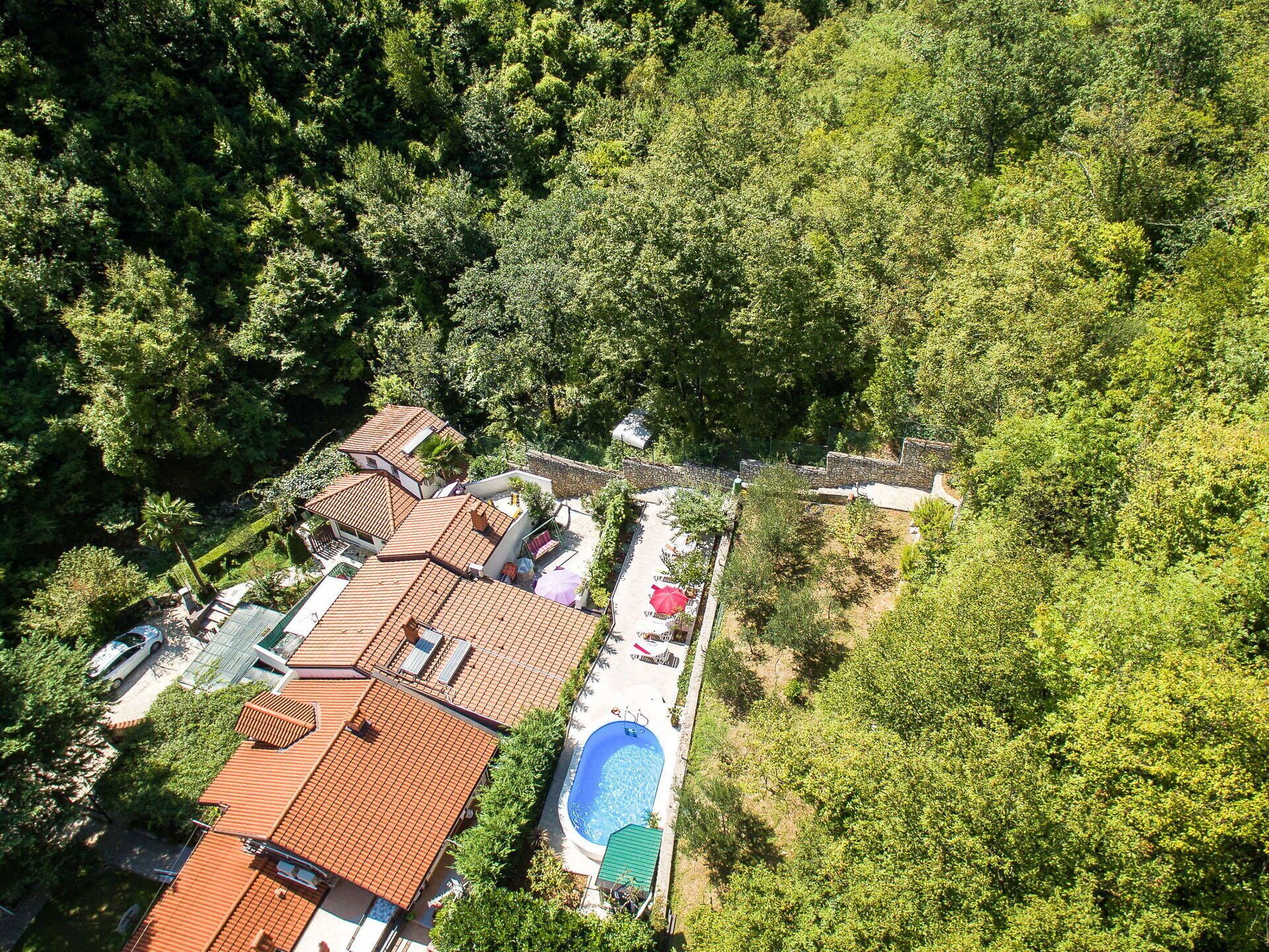 An aerial view of a residential area with multiple houses, a swimming pool, and lush greenery.