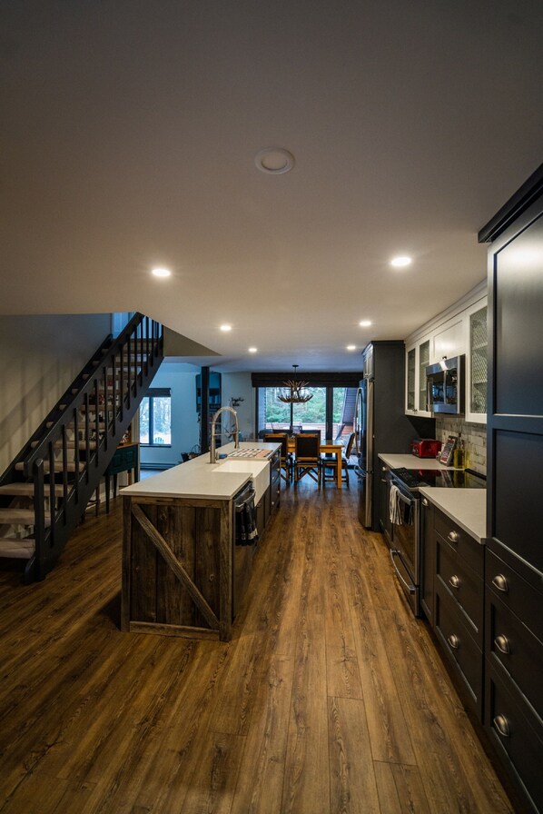 A modern kitchen with dark cabinetry, a wooden island, and a dining area with a view.