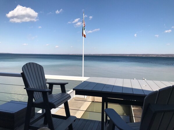 Une terrasse avec des fauteuils Adirondack et une table, offrant une vue sur une mer calme et un ciel dégagé.