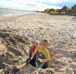 Two children playing in a sandpit on a beach with a clear sky and a distant lighthouse. - Beach House- 3 blocks to beach, Huge patio, Sauna, Fire Pit and 2 bikes! 🚲🔥🌊 (Two Rivers)