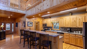 A spacious kitchen with wooden cabinetry, a central island with bar stools, and a second-story balcony. - Stress Re-Leaf - Blowing Rock Cabin with great view, hot tub, pool table (Lenoir)