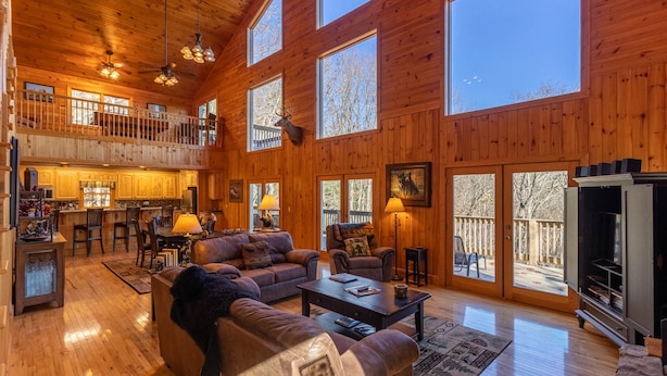 A spacious wooden cabin with a dining area, a living room with sofas and a fireplace, and large windows offering views of the outdoors. - Stress Re-Leaf - Blowing Rock Cabin with great view, hot tub, pool table (Lenoir)