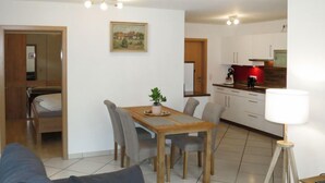 Ein modernes Wohnzimmer mit einer Couch, einem Esstisch und Stühlen. Es gibt eine Küchenzeile mit Schränken und einer Lampe.