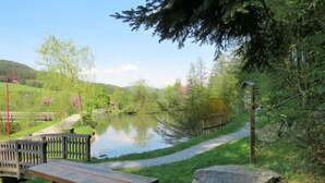 Ein Picknickbereich mit Bänken und einer Holzbrücke über einem ruhigen Fluss, umgeben von Grünpflanzen und Bäumen.