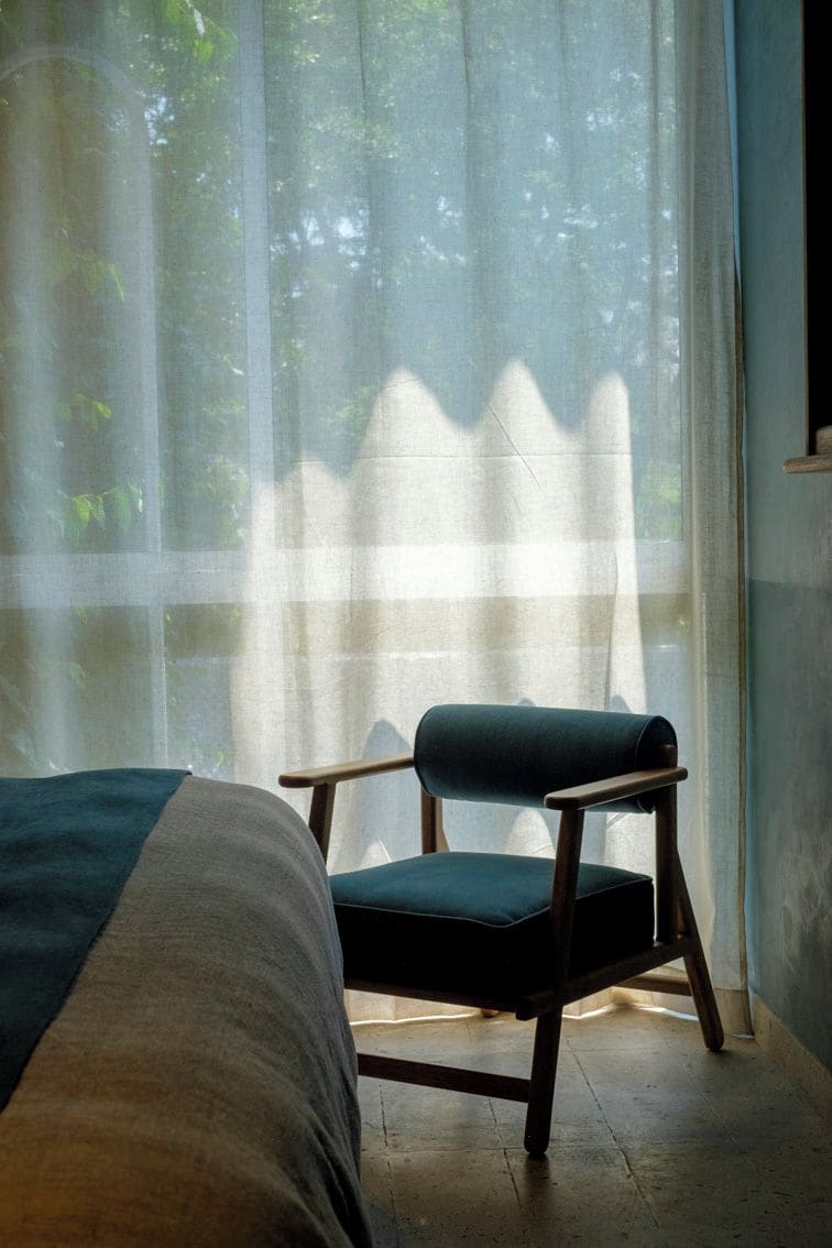 A room with a bed, a chair, and a large window with sheer curtains.