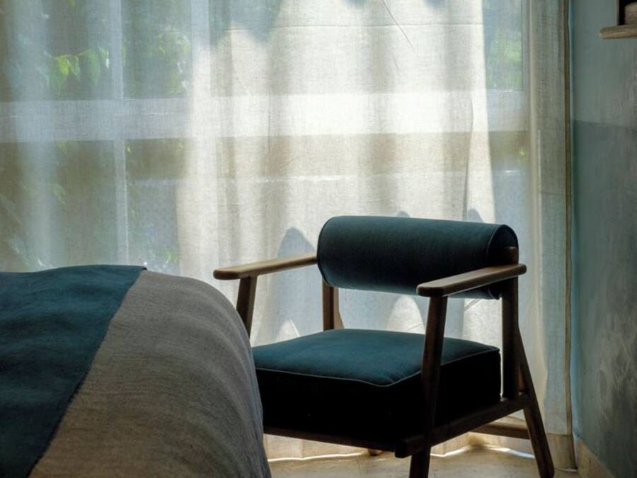 A room with a bed, a chair, and a large window with sheer curtains.
