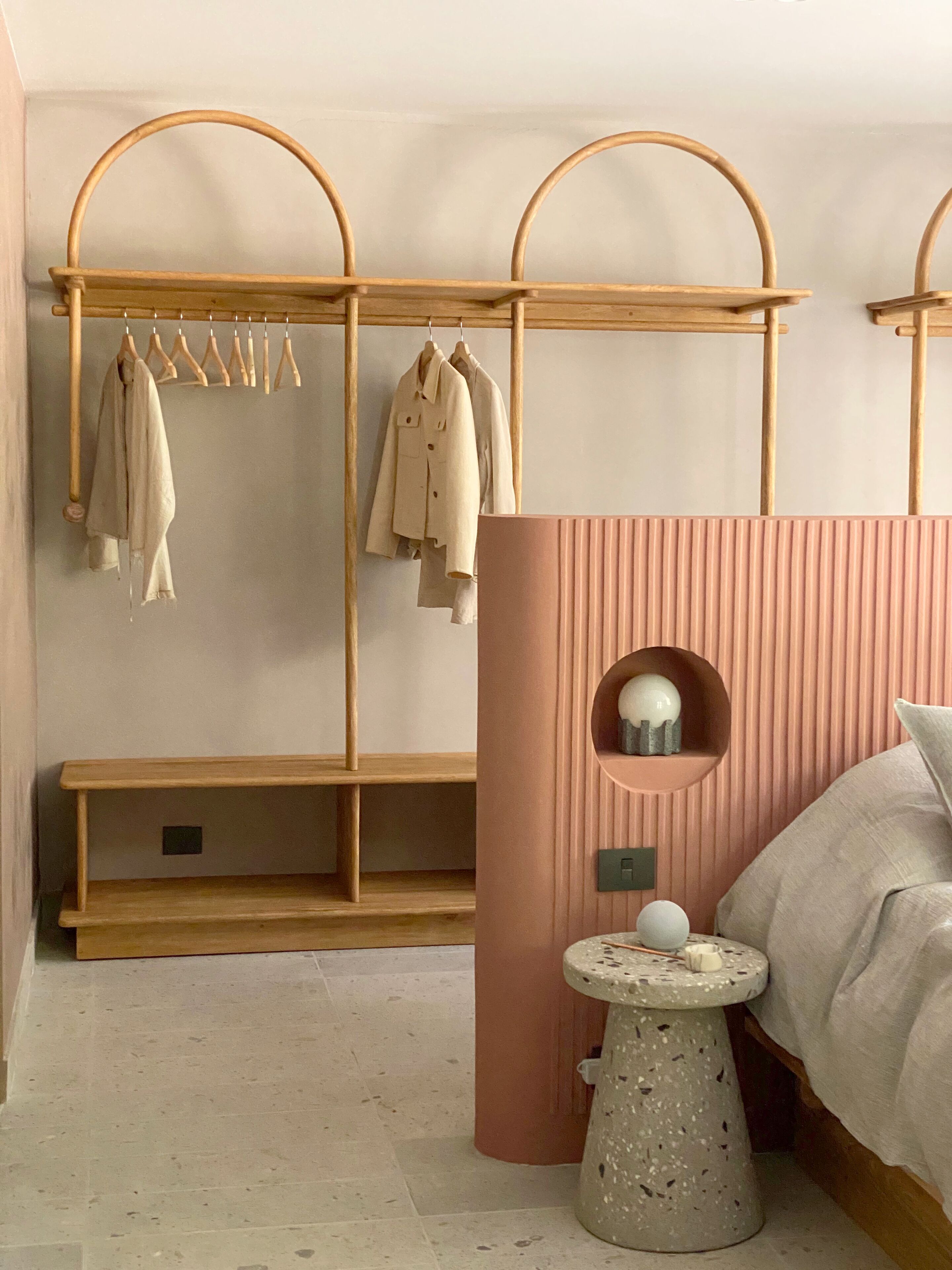 A bedroom with a wooden bench, a pink wall panel, and a bedside table with a decorative object.